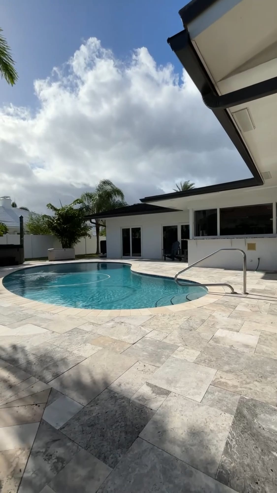 Pool and travertine deck behind a single storey home in Sea Ranch Lakes